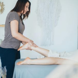 A Woman in Gray Shirt Massaging a Leg of a Person Lying Down